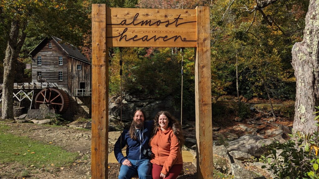 Two people sitting in a swing with an Almost Heaven sign above them at Babcock State Park, one of the top west virginia state parks
